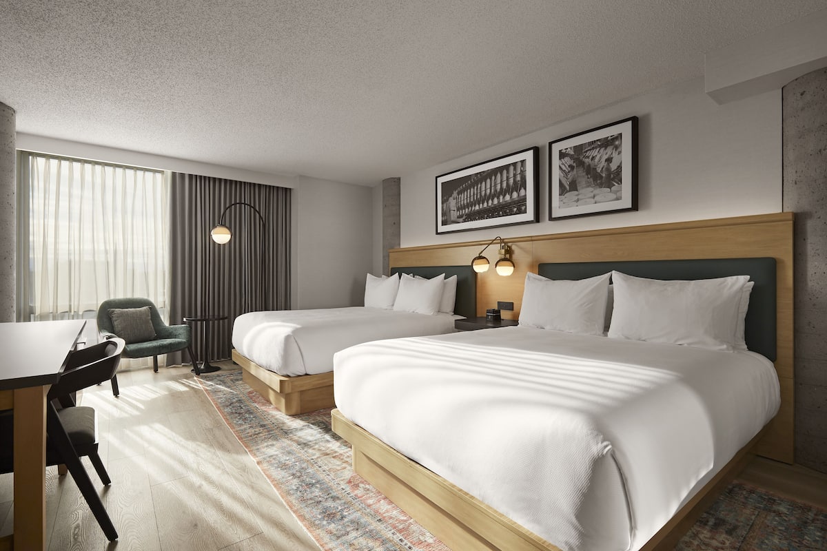 A hotel room with two beds, a desk, a chair, and a large window with curtains.