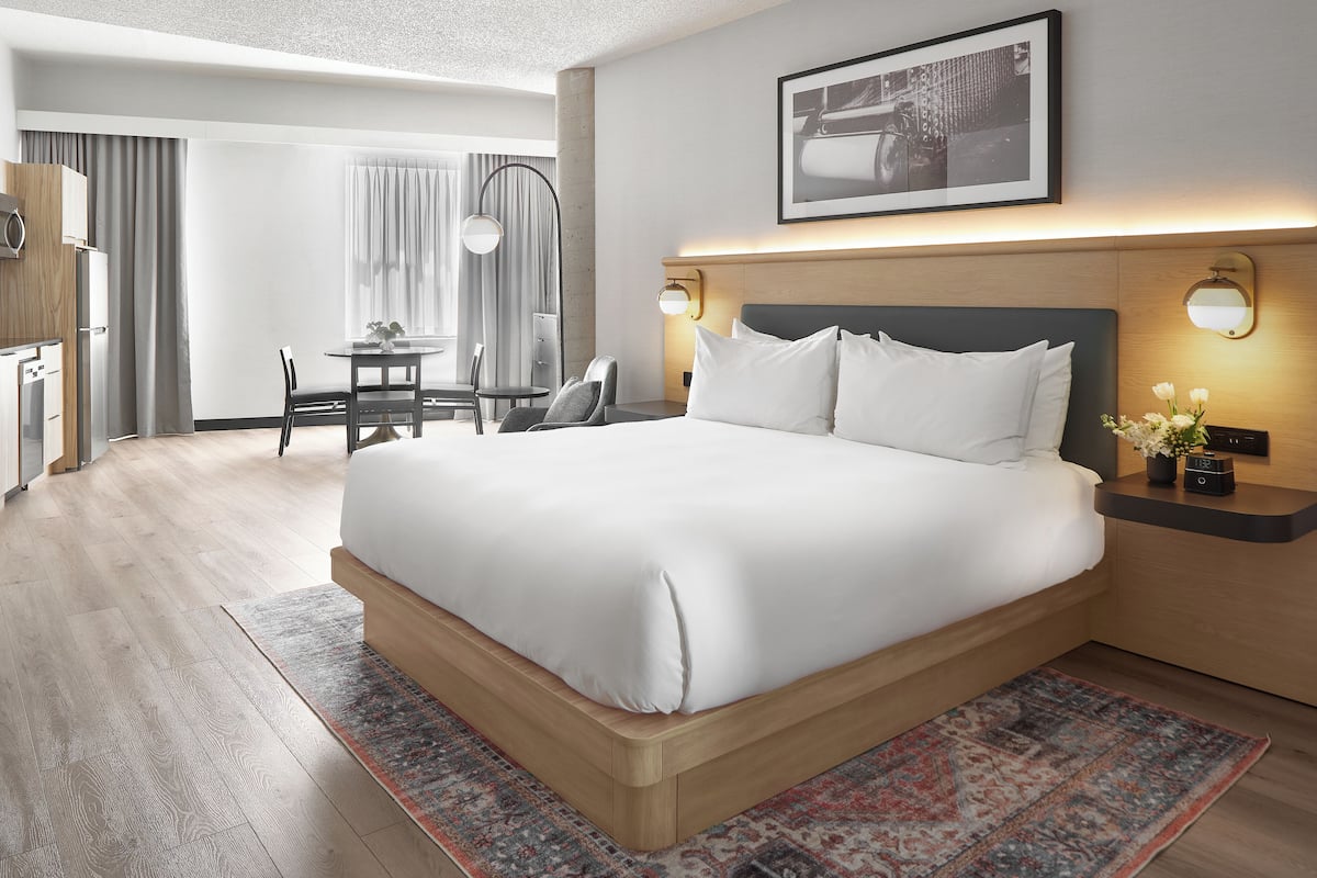 A hotel room with a large bed, a desk, a chair, and a dining table.