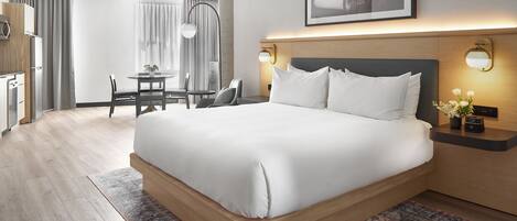 A hotel room with a large bed, a desk, a chair, and a dining table.