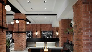 A modern interior with exposed brick walls, a black bar counter, and a seating area with two chairs and a table. - Hôtel MOCO Valleyfield (Salaberry De Valleyfield)