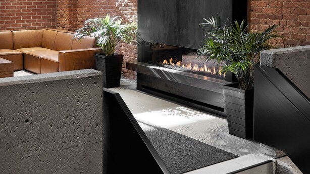A modern lounge area with a brick wall, a large fireplace, and a seating area with a sofa and plants. - Hôtel MOCO Valleyfield (Salaberry De Valleyfield)