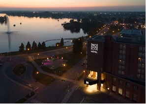 A hotel with a prominent sign, a waterfront view, and a roundabout with traffic lights. - Hôtel MOCO Valleyfield (Salaberry De Valleyfield)