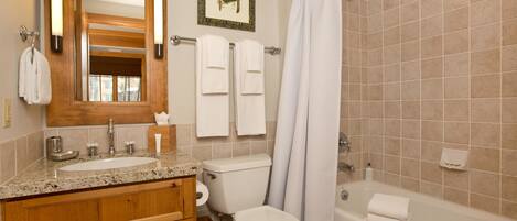 A bathroom with a sink, toilet, and bathtub. There are towels hanging on the wall and a framed picture above the mirror.