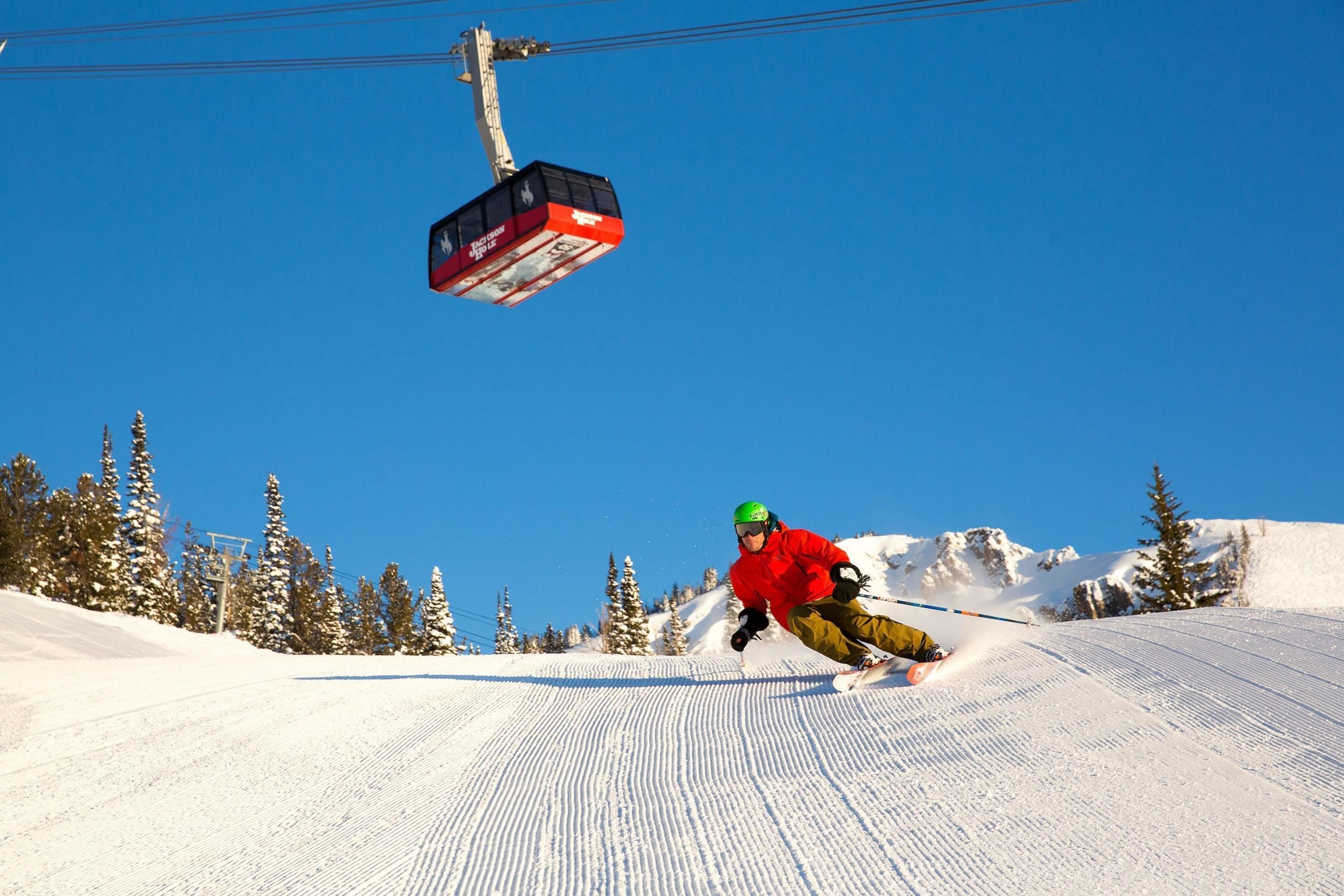 A person skiing down a snowy slope with a ski lift in the background.