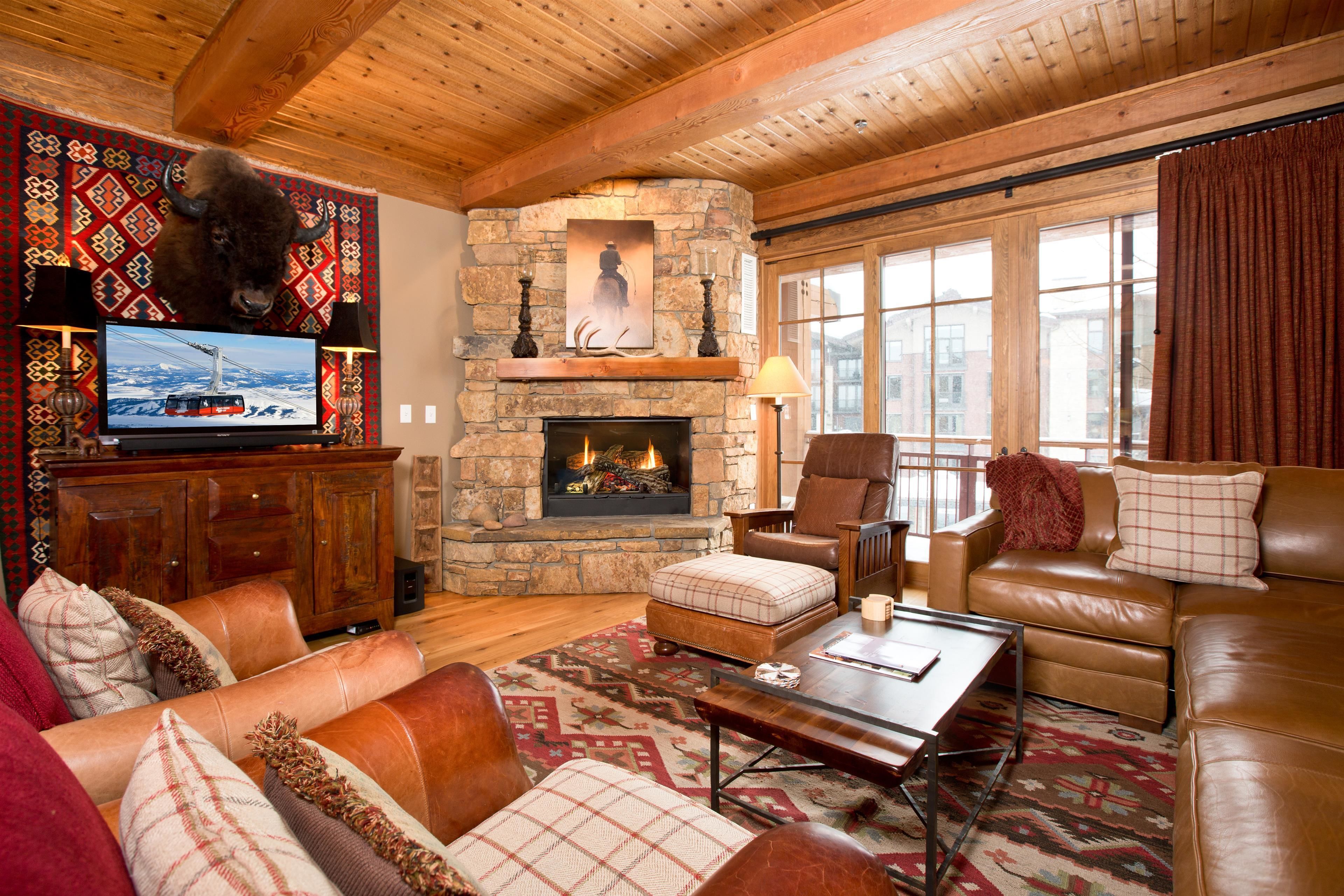 A cozy living room with a stone fireplace, leather sofas, and a television displaying a snowy landscape.