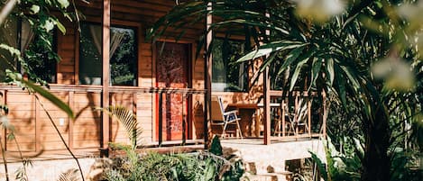 A wooden cabin with a porch, surrounded by lush greenery.