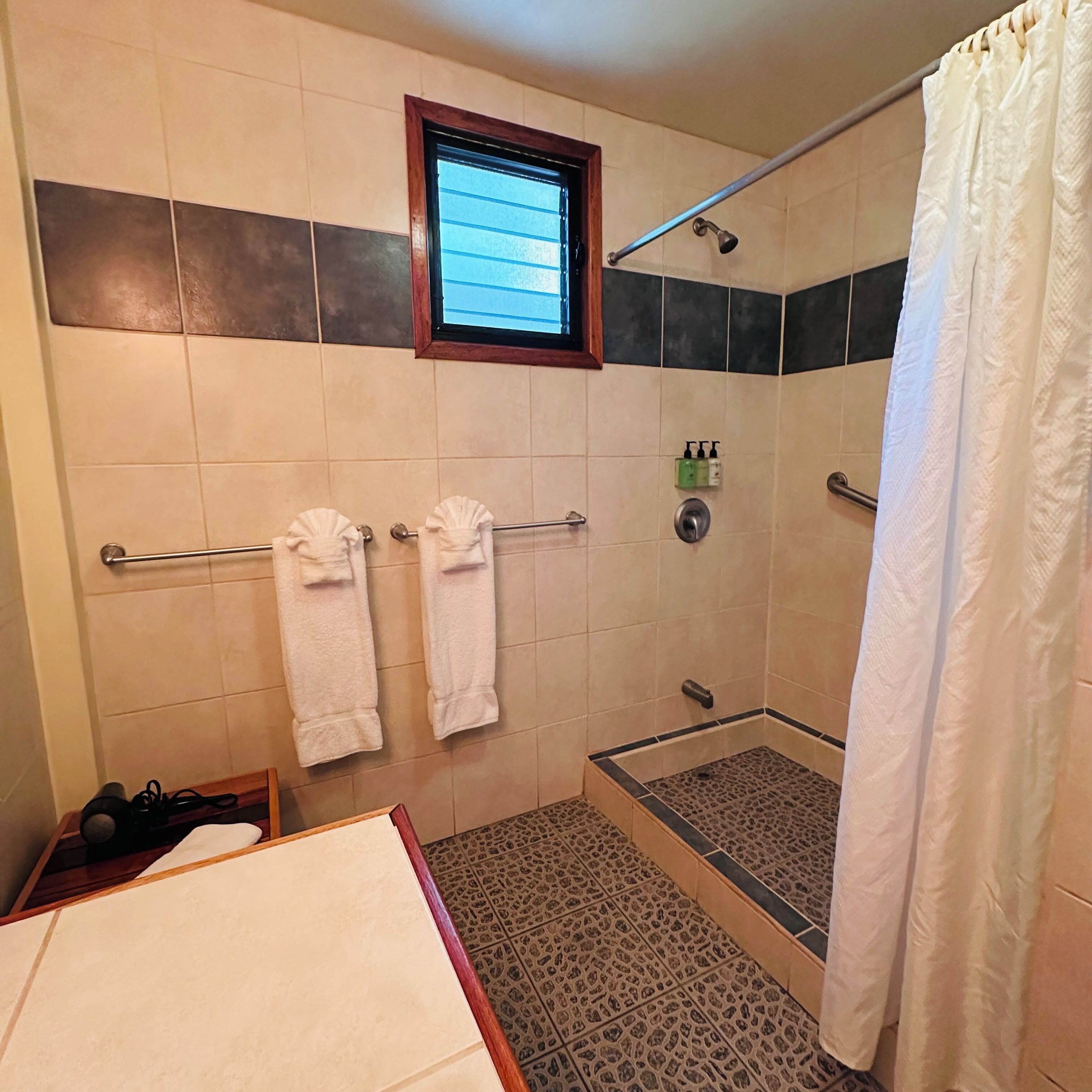 A shower area with a glass door, a towel rack with two towels, and a window above the shower.