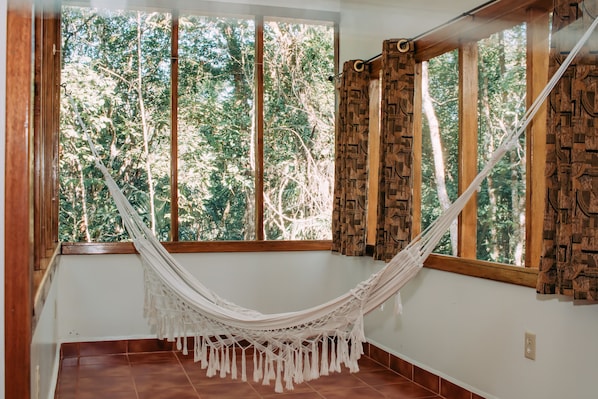 Una hamaca en una habitación con ventanas amplias y cortinas estampadas.