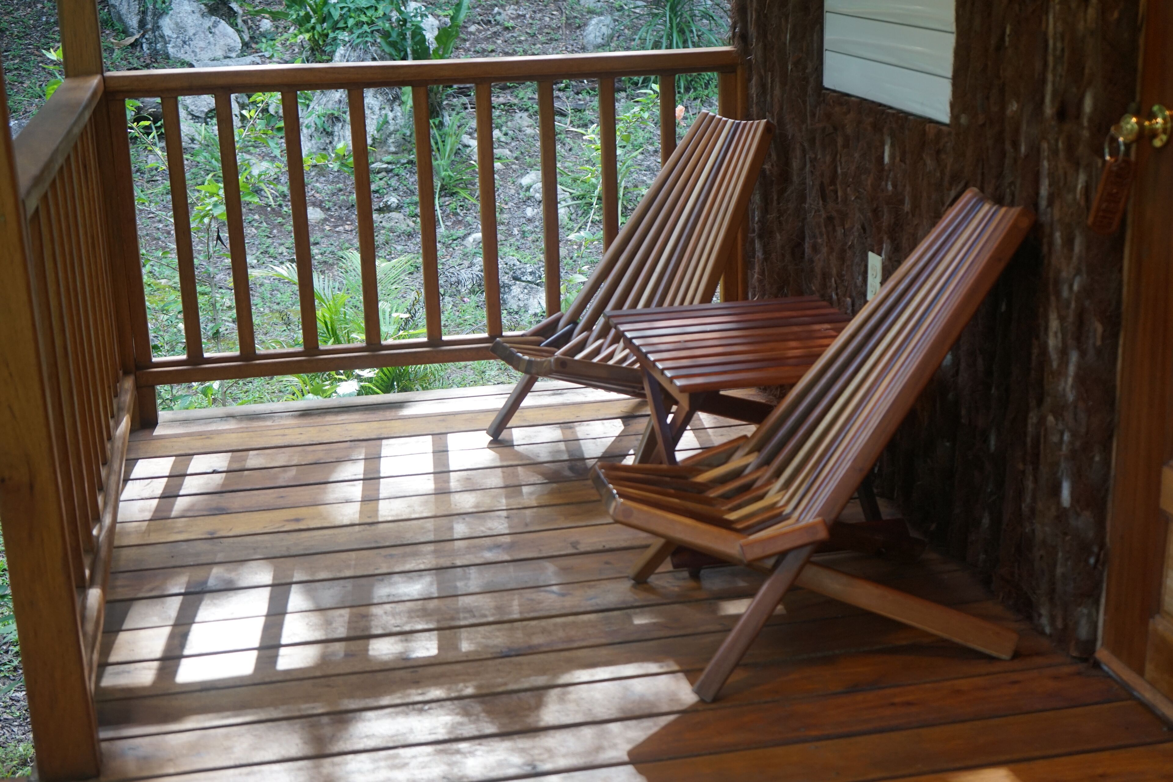 Terraza de madera con dos sillones de descanso y vista a follaje.