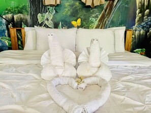 Una cama con dos toallas con forma de serpientes, un adorno de mariposa y un mural de un bosque en la pared.