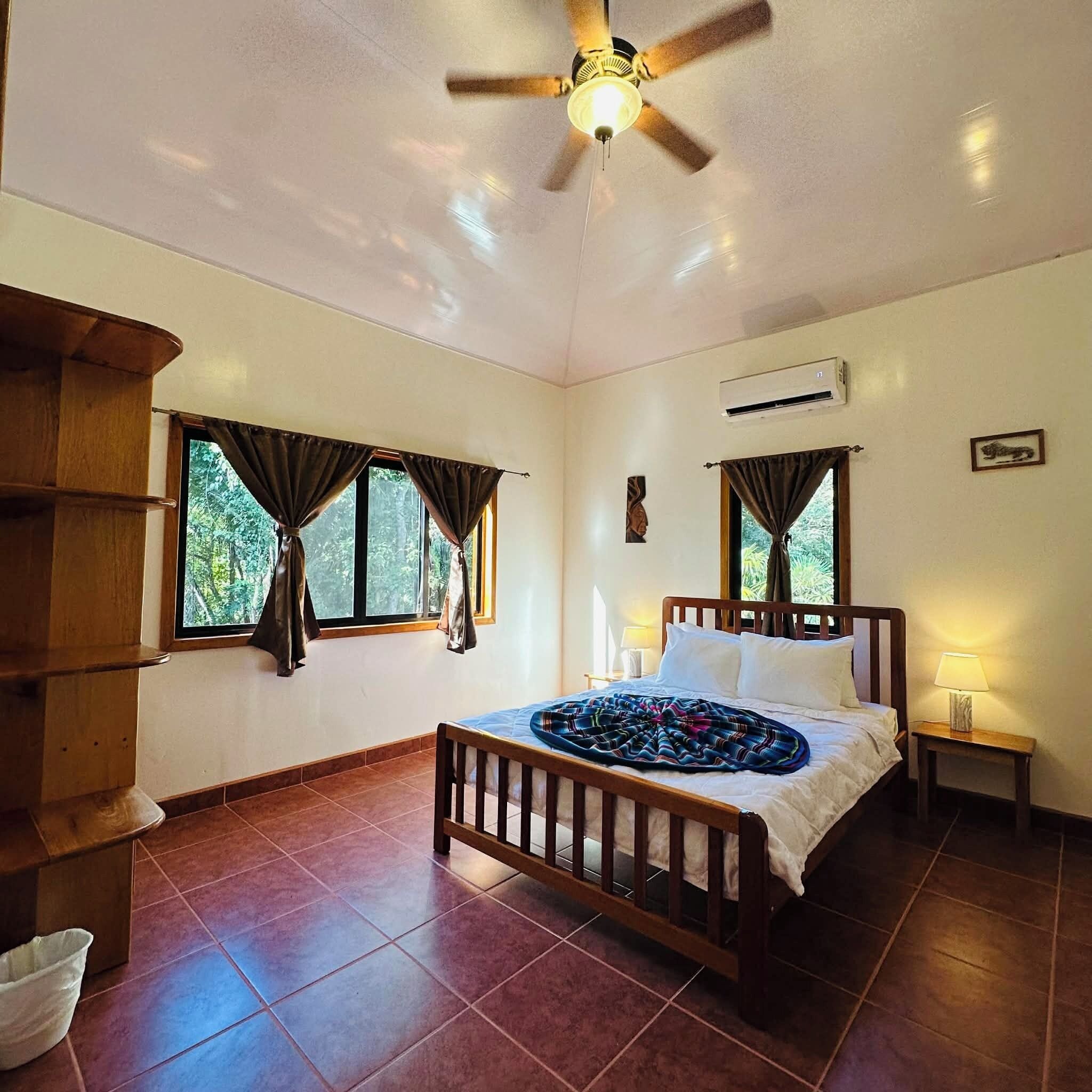 A bedroom with a wooden bed, two bedside tables, a ceiling fan, and windows with curtains.