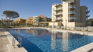 Une piscine à l’eau d’un bleu cristallin, entourée de bâtiments modernes dotés de balcons, avec un arbre en premier plan.