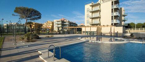 A swimming pool with a modern pool deck, surrounded by buildings and a clear sky.