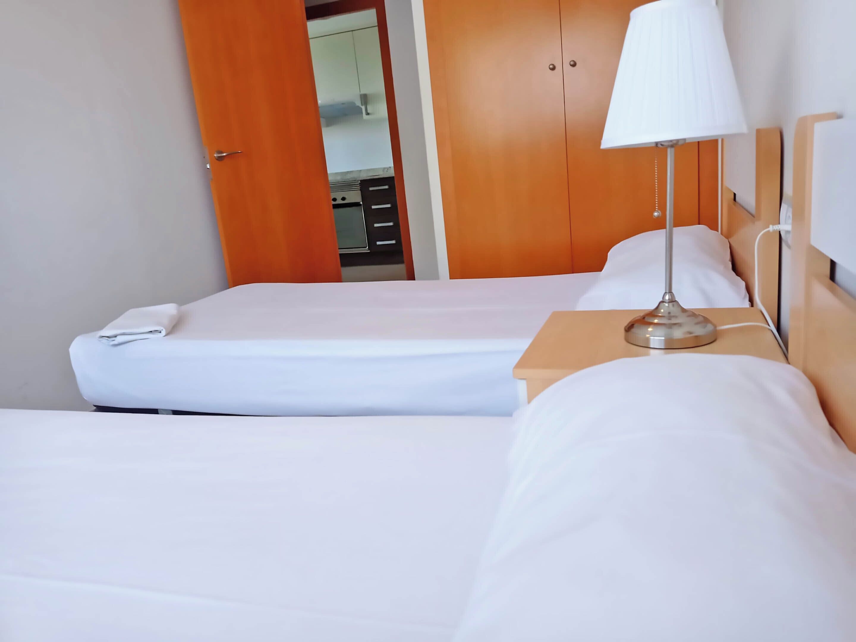 Une chambre d’hôtel avec deux lits, une table de chevet avec une lampe et une armoire.