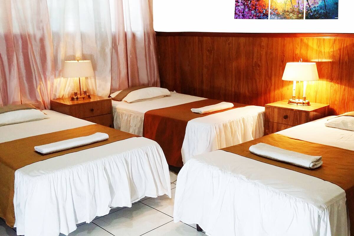 Ein Hotelzimmer mit zwei Einzelbetten, jeweils mit weißer Bettdecke und ordentlich gefaltetem Handtuch. Es gibt Nachttische aus Holz mit Lampen und ein Holz-Kopfteil.