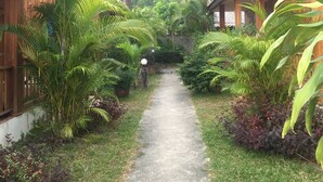 A pathway leading to a row of wooden buildings with tiled roofs, surrounded by lush greenery and a hilly backdrop. - Poonsap Resort (Ko Lanta)