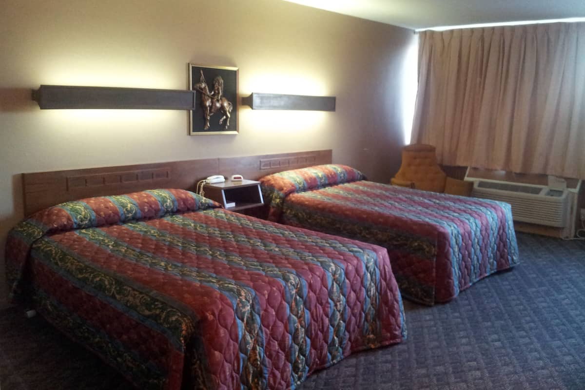 A hotel room with two beds, a nightstand, a wall-mounted TV, and a window with curtains.