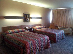 A hotel room with two beds, a nightstand, a wall-mounted TV, and a window with curtains. - Indian Head Motel (Winamac)