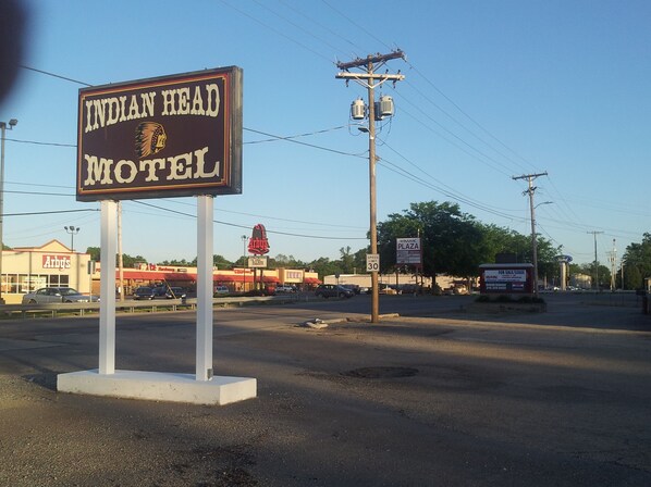 A sign for the Indian Head Motel with a clear view of the surrounding area including a speed limit sign, a Winamac Plaza sign, and a Ford dealership in the background. - Indian Head Motel (Winamac)