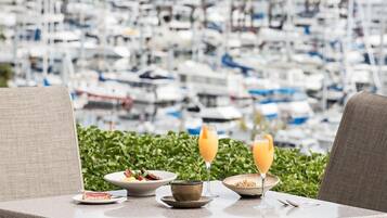 A table with breakfast items and drinks, overlooking a marina with boats.