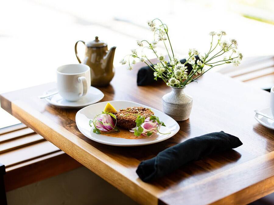 A wooden table with a white plate of food, a teapot, a cup, and a vase with flowers.