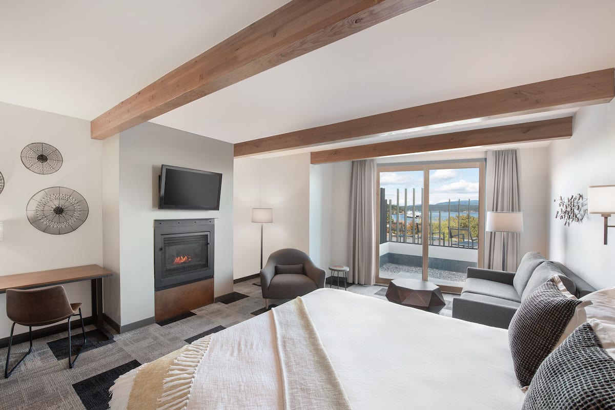 A hotel room with a fireplace, a TV, a bed, a desk, and a balcony with a view of the sea.
