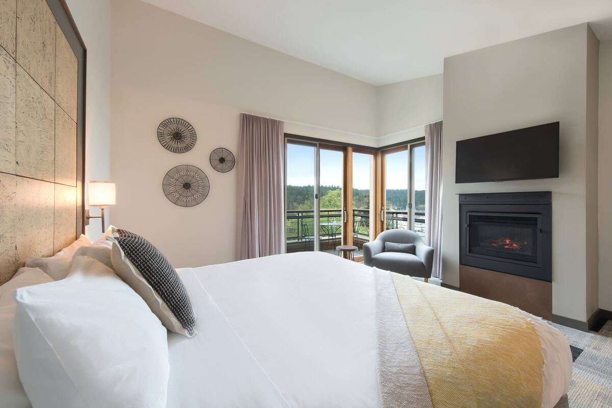A hotel room with a large bed, a fireplace, a TV mounted on the wall, and a view of the outdoors.