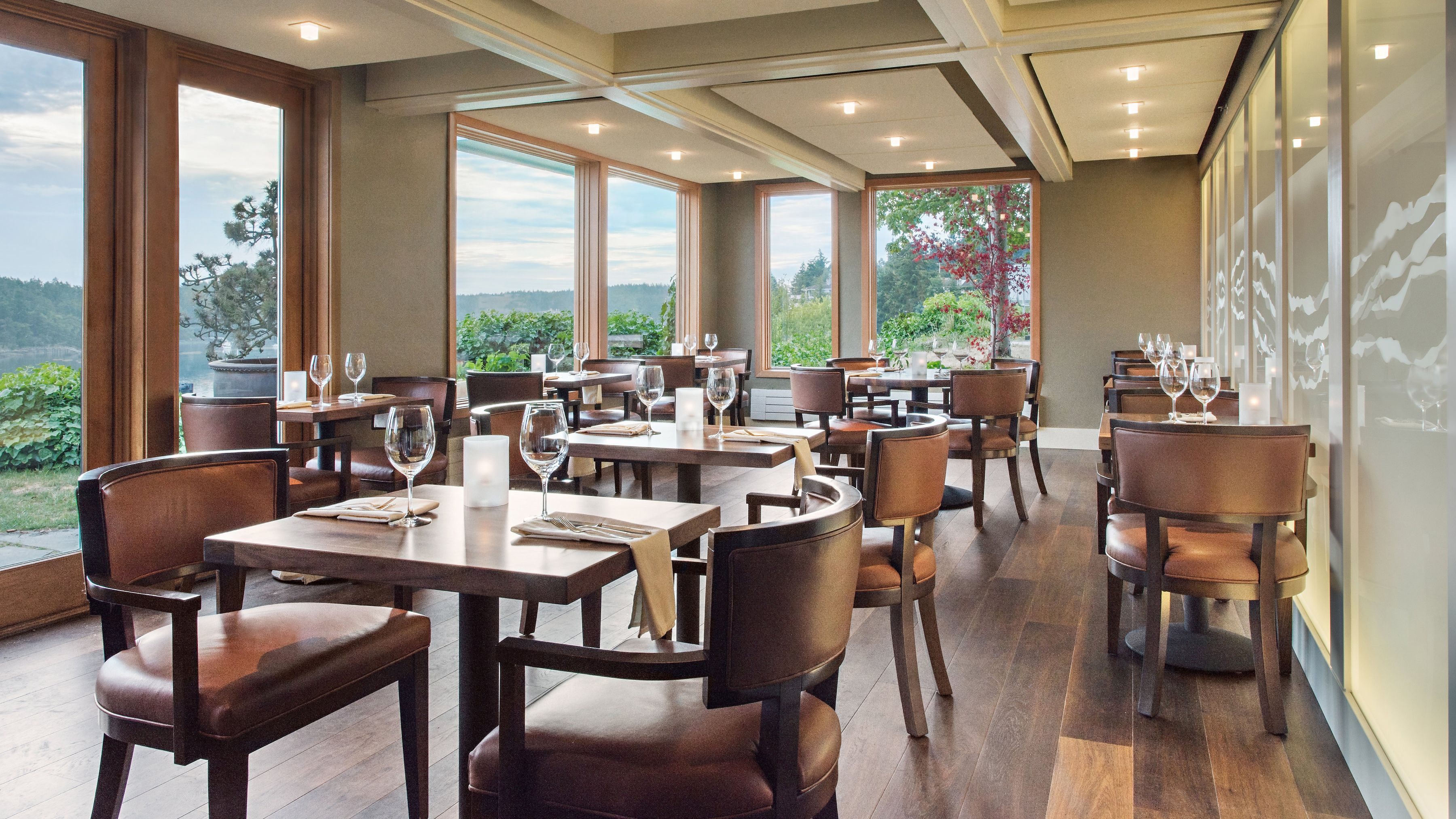 A restaurant with multiple tables and chairs, large windows offering a view of greenery and hills, and a modern interior design.