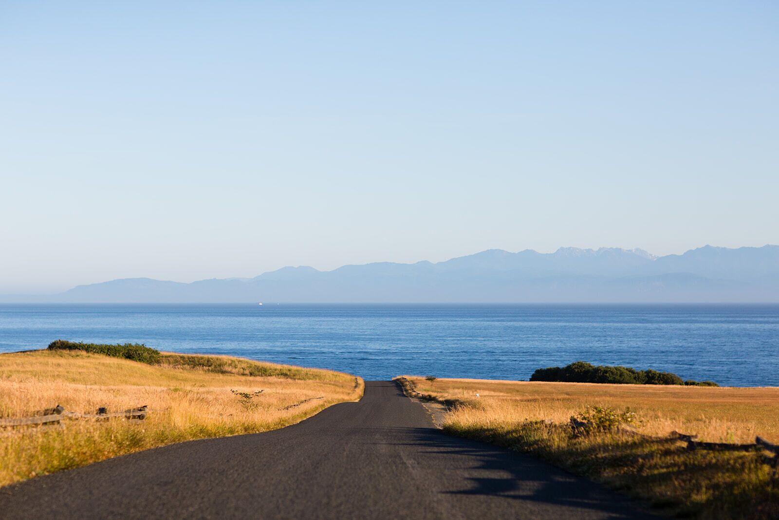 A road leading to a body of water with mountains in the background.