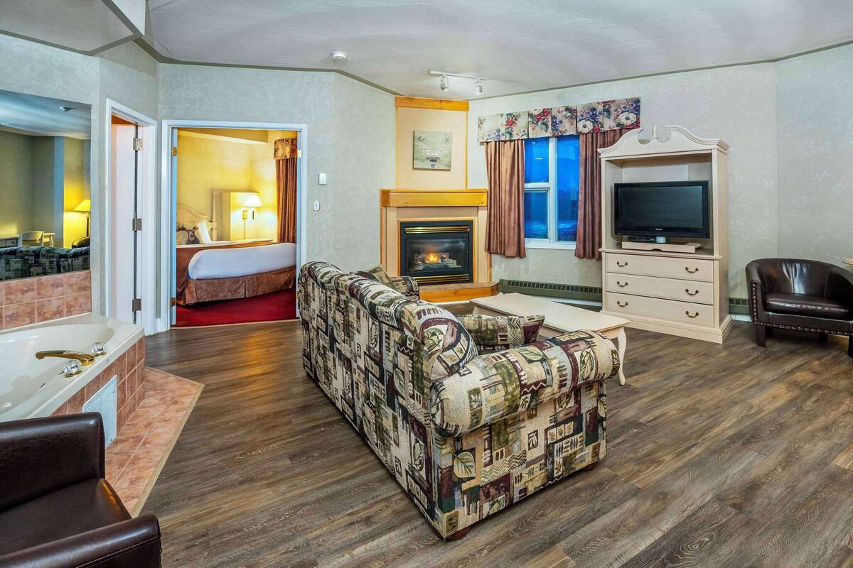 A living room with a fireplace, sofa, TV stand, and a separate bedroom with a bed and bathroom.