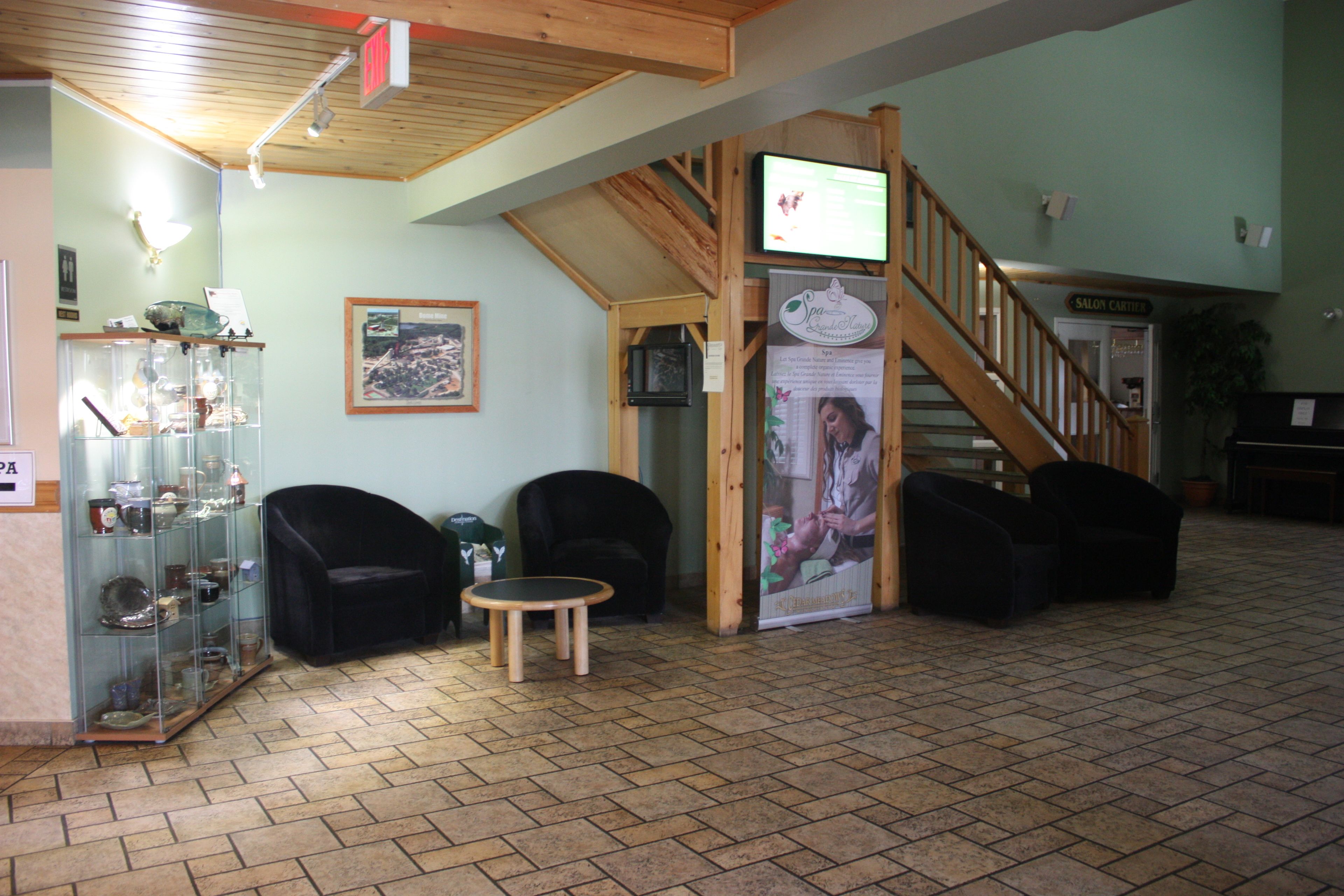A lobby with a reception desk, two black armchairs, a small wooden table, a glass display case, a staircase, and a sign for a salon.