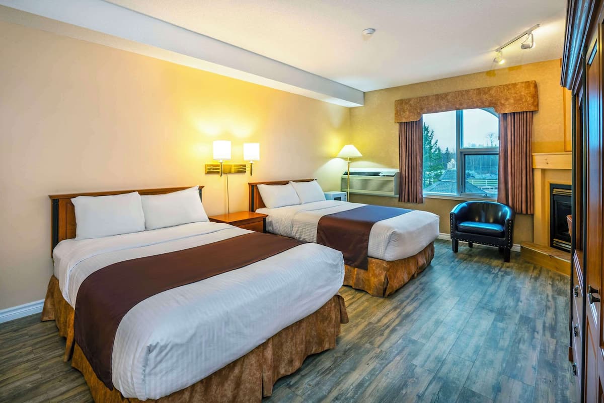 A hotel room with two beds, a fireplace, a window with curtains, and a chair.