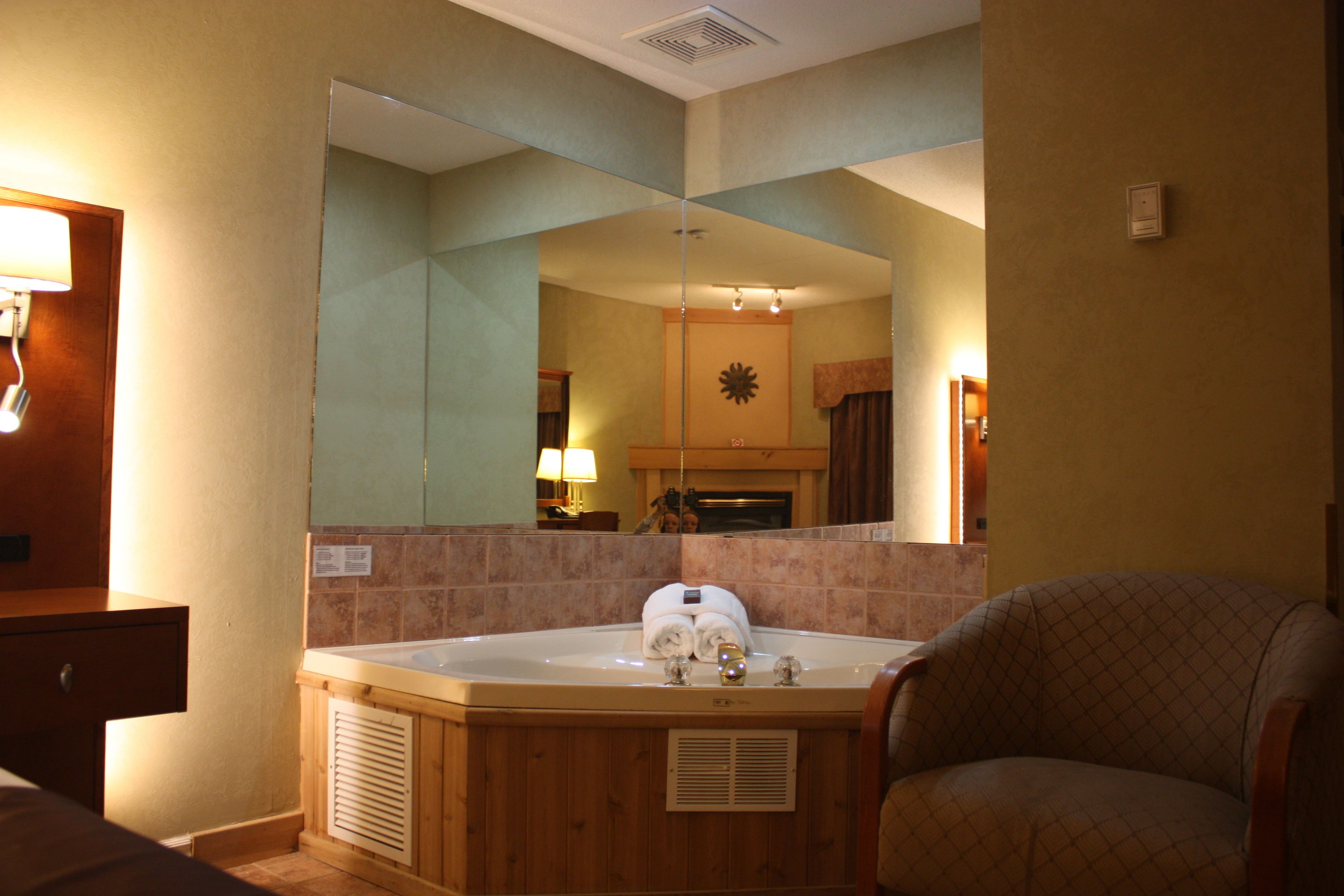 A bathroom with a large mirror, a bathtub, a chair, and a sink.