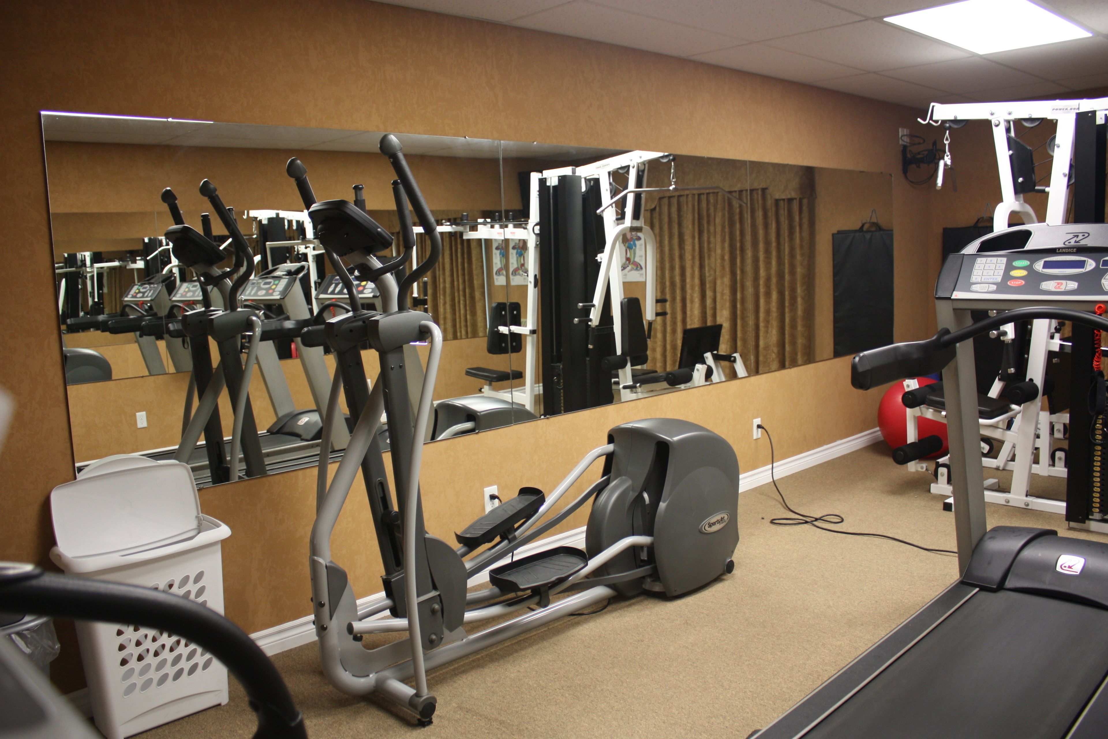 Une salle de sport équipée de matériel d’exercice, d’un miroir et d’un tapis de course.