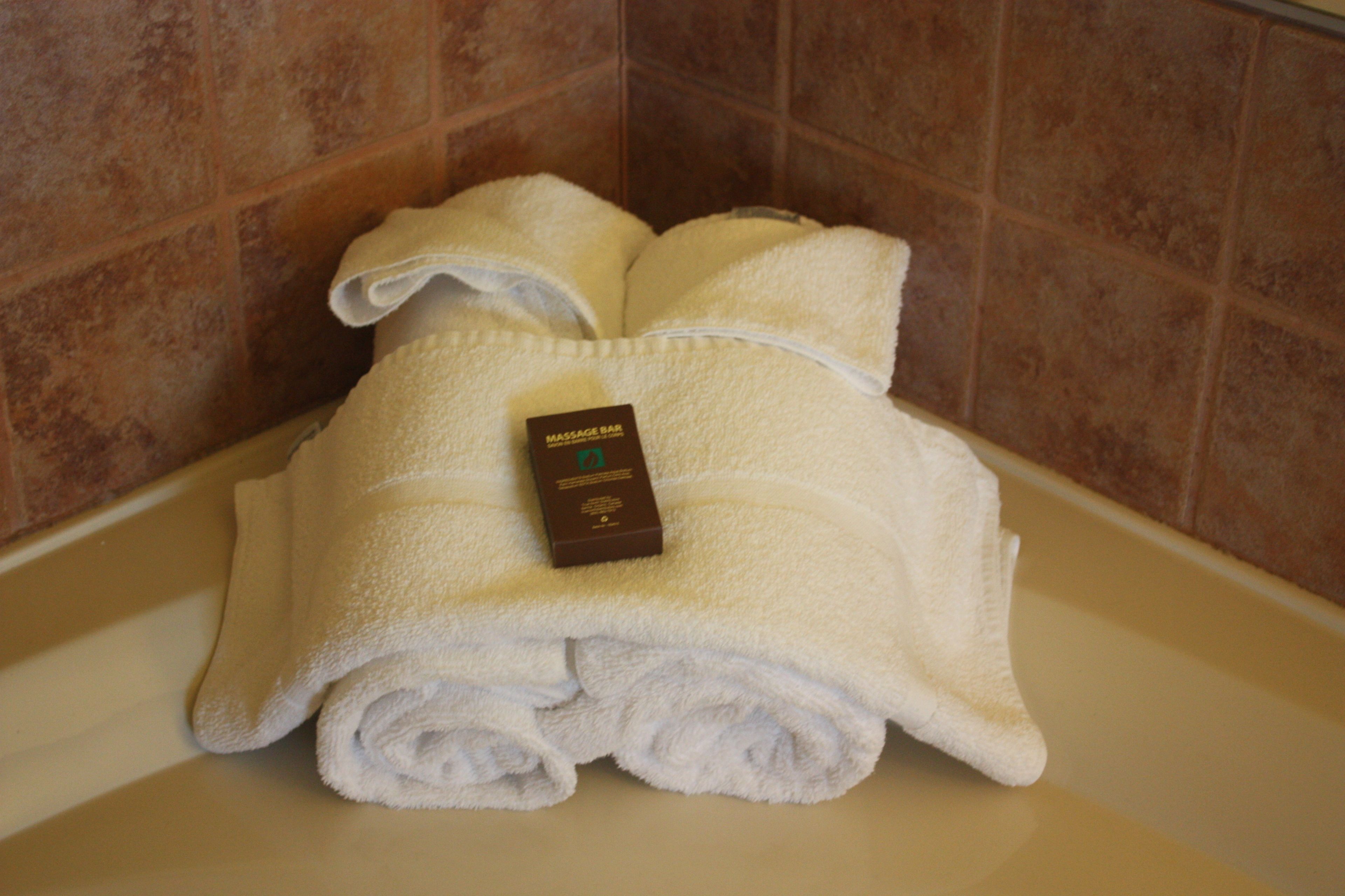 A stack of white towels with a massage bar tag on a bathtub.