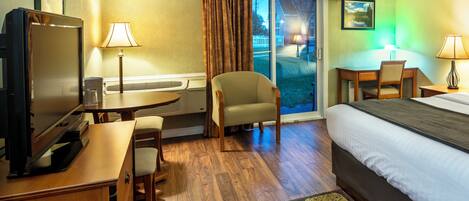 Habitación de hotel con cama, escritorio, silla, televisor y vistas al exterior.