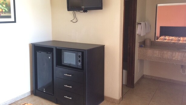 A room with a flat-screen TV mounted on the wall, a kitchenette with a microwave, and a small refrigerator. - Bayshore Motel (La Porte)