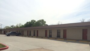 A motel with a row of single-story buildings, each with a red door and a small window. - Bayshore Motel (La Porte)