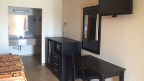A room with a bed, a desk, a chair, a mirror, and a television. - Bayshore Motel (La Porte)