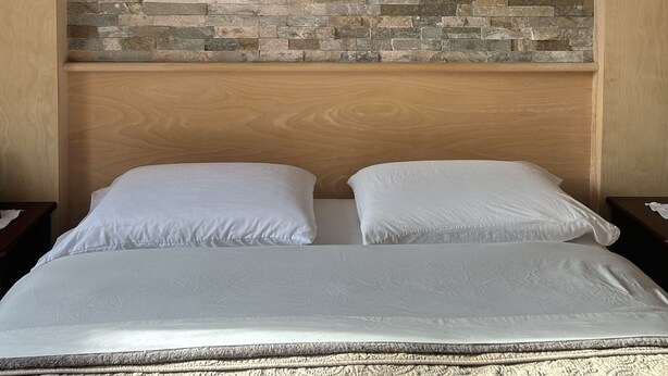 A bed with a headboard featuring a stone wall design, two white pillows, and a textured bedspread. - Le Sieur de Joliette (Montreal)