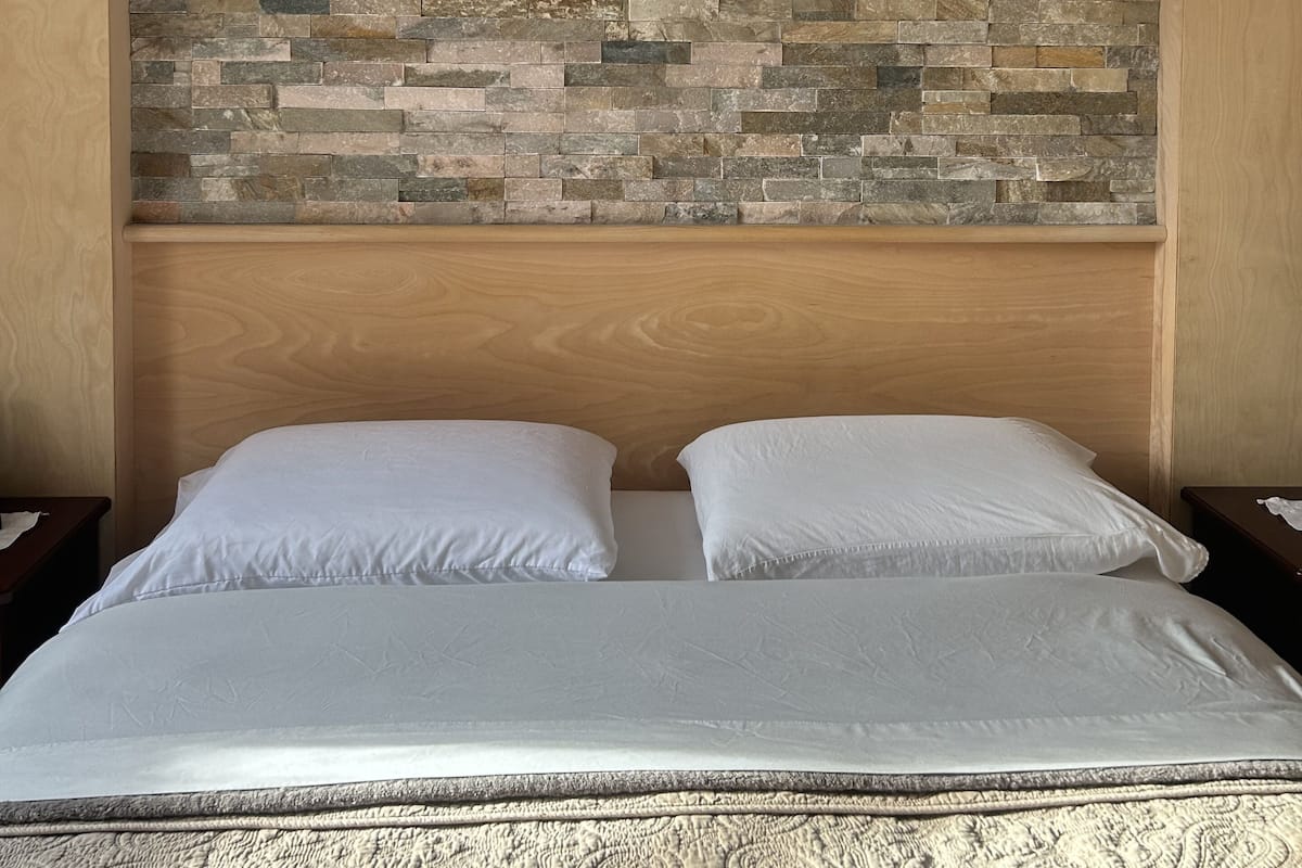 Un lit doté d’une tête de lit ornée d’un motif mural en pierre, de deux oreillers blancs et d’une couvre-lit à texture.