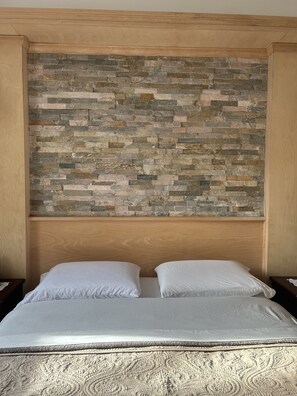 Een bed met hoofdbord, vormgegeven als een stenen muur, twee witte kussens en een beddegoed met structuur.