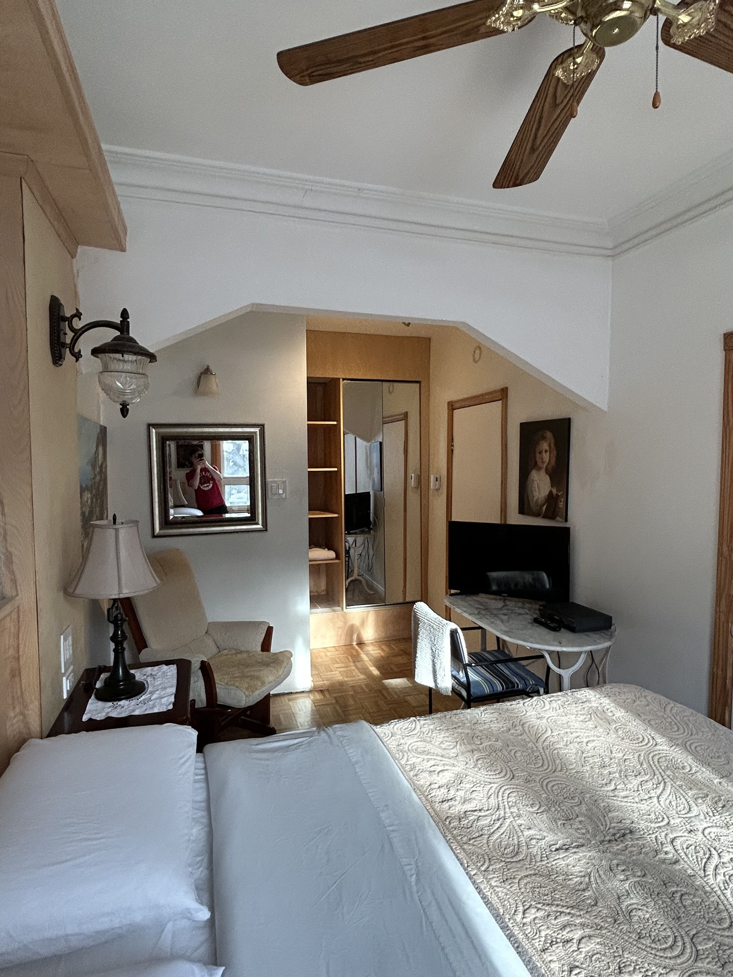 Ein Hotelzimmer mit zwei Betten, einem Deckenventilator, einem Schreibtisch mit Stuhl, einer Lampe, einem Spiegel und einem Kleiderschrank.