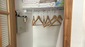 A compact laundry room with a stacked washer and dryer, wooden hangers, and neatly folded towels.