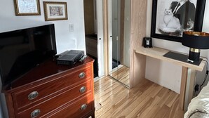 A bedroom with a wooden dresser, a TV, a framed picture, and a bedside table with a lamp. - Le Sieur de Joliette (Montreal)