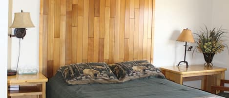 A bedroom with a wooden headboard, a bed with a green bedspread, two bedside tables with lamps, and a small wooden desk with a plant.