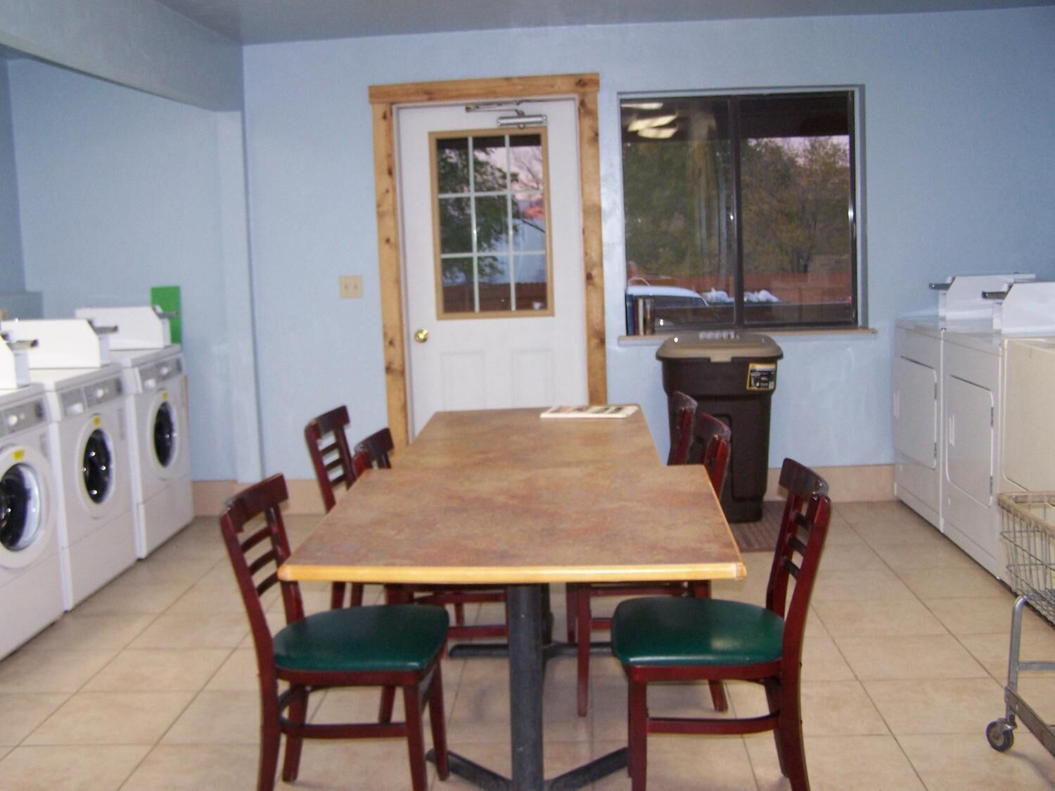 Un comedor con una mesa de madera y cuatro sillas, una puerta con ventana y una lavadora a la izquierda.