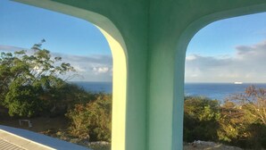 Vista a través de un arco verde que da a un paisaje costero con árboles y el océano.