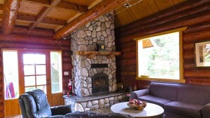 A cozy cabin interior with a stone fireplace, leather furniture, and a large window offering a view of the outdoors. - Handsome Dan's at Otter Point (Juan de Fuca Electoral Area)