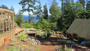 A rustic cabin with a wooden deck and a glass enclosure, surrounded by dense forest and a view of the ocean. - Handsome Dan's at Otter Point (Juan de Fuca Electoral Area)